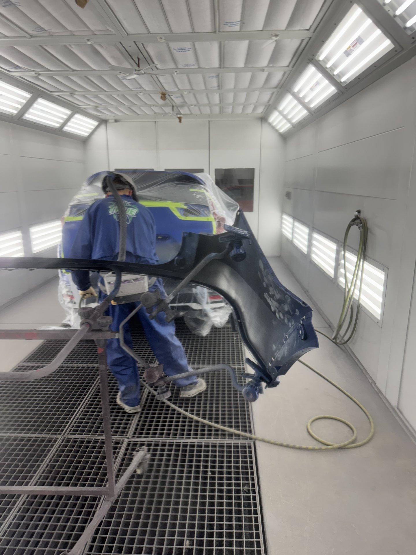 Paint technician spraying Aegean Blue Metallic paint on a 2021 Honda CR-V inside the downdraft paint booth at Bob Rohrman Collision Repair Center in Lafayette, Indiana