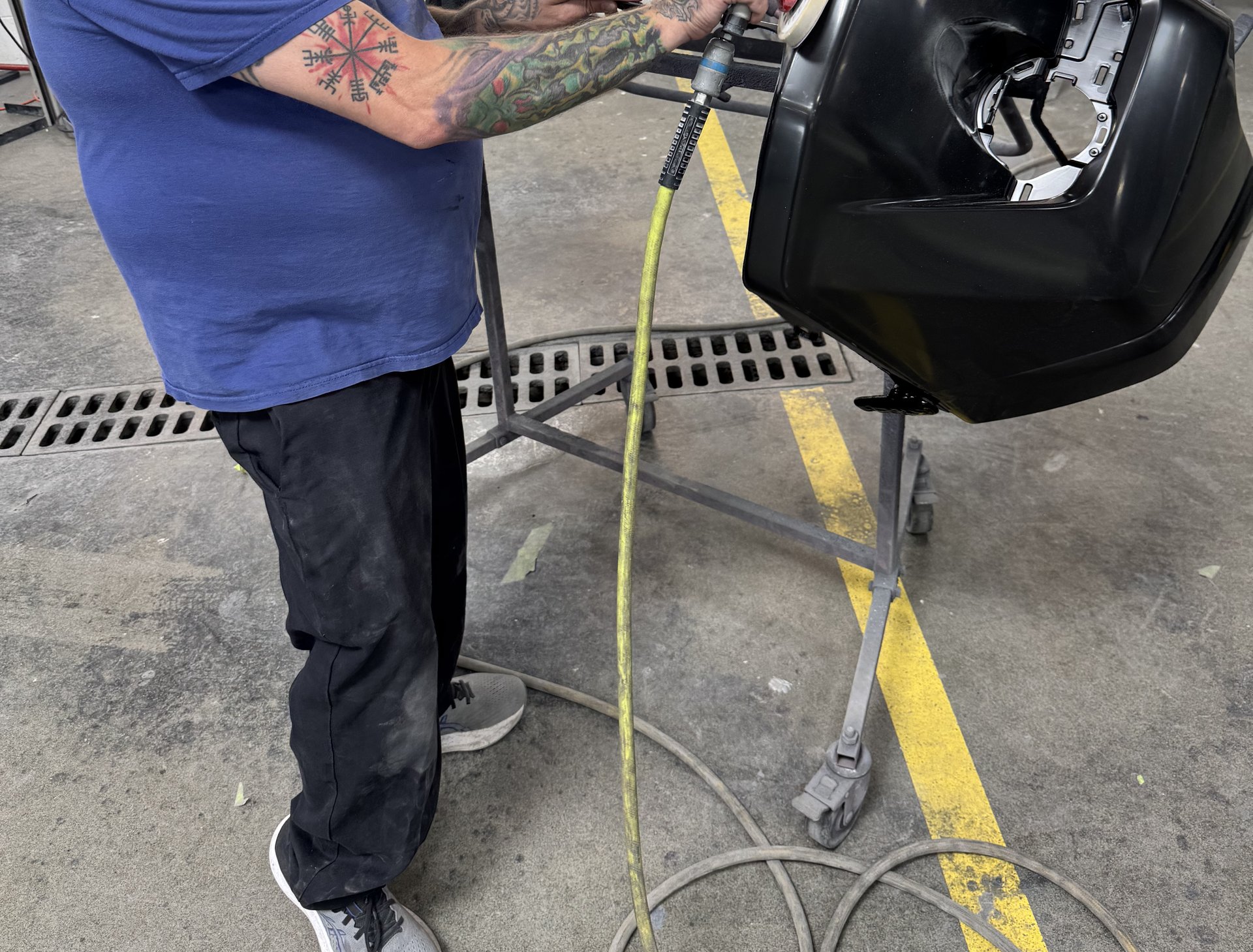 Body technician DA sanding a black bumper cover with a 3M dual-action sander to prep the surface for paint at Bob Rohrman Collision Repair Center in Lafayette, Indiana